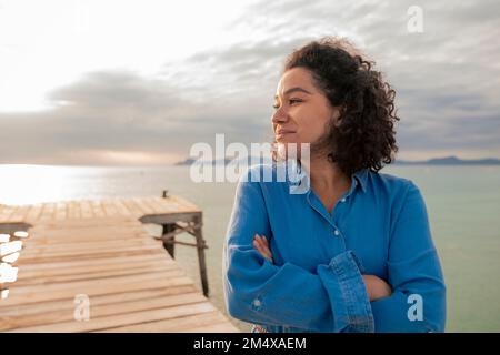 Femme souriante et attentionnée debout sur la jetée au coucher du soleil Banque D'Images