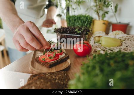 Homme faisant un sandwich avec des microverts maison dans la cuisine à la maison Banque D'Images