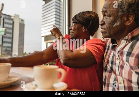 Femme souriante pointant par un homme au café Banque D'Images