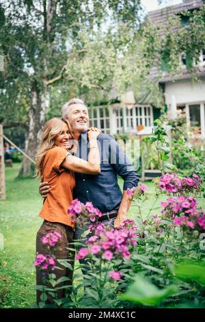 Bonne femme embrassant homme debout par les plantes à fleurs Banque D'Images