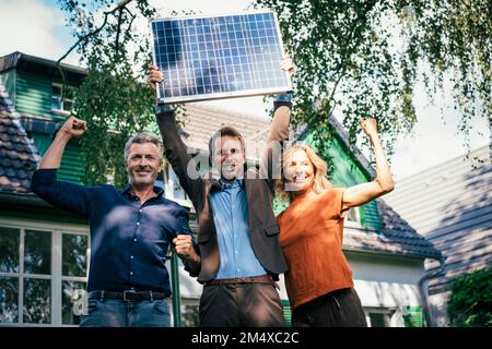 Homme heureux et femme flexion des muscles avec agent immobilier charge panneau solaire par la lumière du soleil Banque D'Images