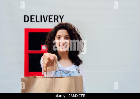 Femme souriante montrant le sac à provisions devant le mur avec l'affiche de livraison Banque D'Images