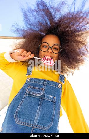 Fille portant des lunettes de vue appréciant manger Lollipop Banque D'Images