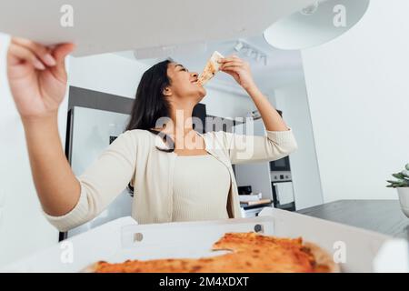Bonne jeune femme mangeant de la pizza à la maison Banque D'Images