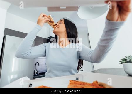 Jeune femme souriante qui mange de la pizza à la maison Banque D'Images