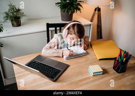 Fille faisant des devoirs assis avec un ordinateur portable sur une table à la maison Banque D'Images