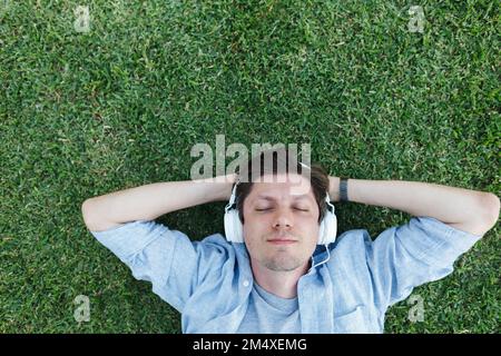 Homme écoutant de la musique avec un casque et se détendant dans l'herbe Banque D'Images