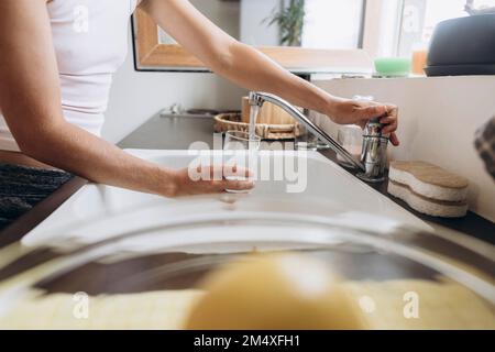 Femme remplissant le verre avec de l'eau du robinet dans la cuisine Banque D'Images