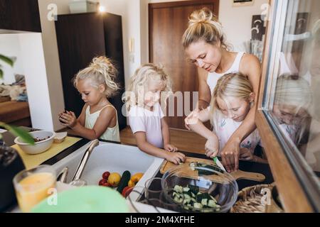 Mère et filles préparant une salade dans la cuisine ensemble Banque D'Images