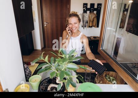 Bonne femme sur le téléphone chargé par la pile solaire dans la cuisine Banque D'Images