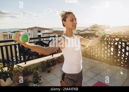 Femme faisant des exercices avec des haltères sur la terrasse du toit au coucher du soleil Banque D'Images