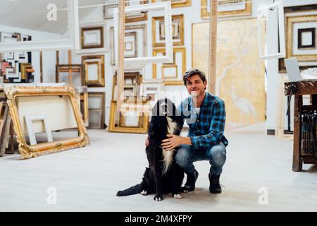 Homme souriant assis avec un chien dans un atelier Banque D'Images