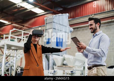 Homme d'affaires heureux avec un collègue portant un simulateur de réalité virtuelle à l'usine Banque D'Images