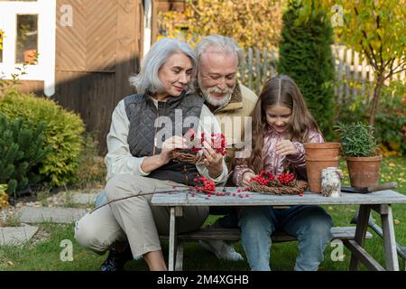 Grands-parents et petite-fille assis à la table de jardin en faisant de la cendre de montagne Banque D'Images