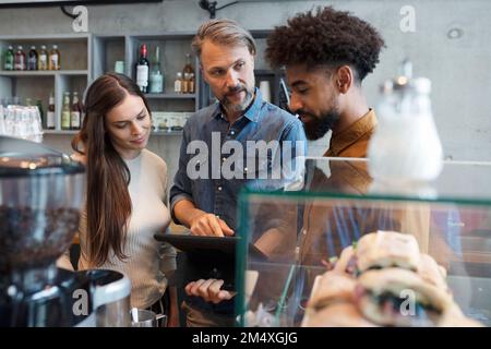 Propriétaire d'un café partageant un Tablet PC avec des baristas dans un café Banque D'Images
