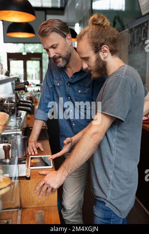 Le propriétaire d'un café partage son Tablet PC avec le barista dans un café Banque D'Images