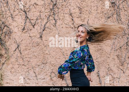 Femme souriante avec les cheveux jetés dansant devant le mur Banque D'Images