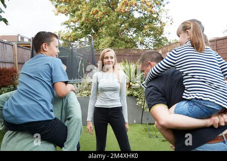 Fille regardant les parents donnant le pigeyback tour aux enfants dans l'arrière-cour Banque D'Images