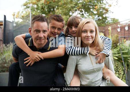 Fille souriante avec un père donnant une promenade en porcgyback à fille et garçon dans le jardin Banque D'Images