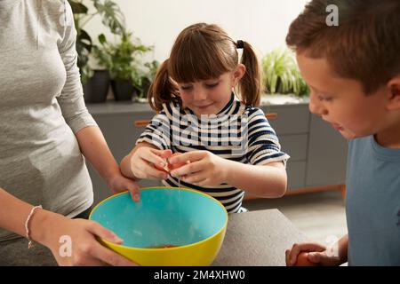 Fille souriante aidant sœur à préparer des biscuits par frère à la maison Banque D'Images