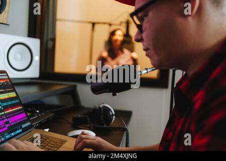 Ingénieur du son composant sur ordinateur portable avec chanteur en arrière-plan au studio d'enregistrement Banque D'Images