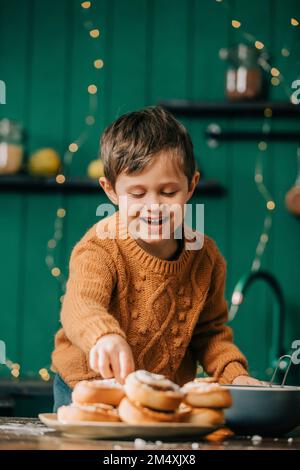 Joyeux garçon avec des petits pains à la cannelle dans la cuisine Banque D'Images