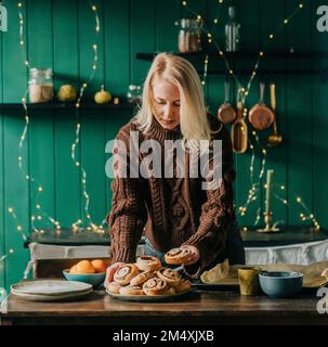 Femme organisant des petits pains à la cannelle sur une assiette sur une table à la maison Banque D'Images