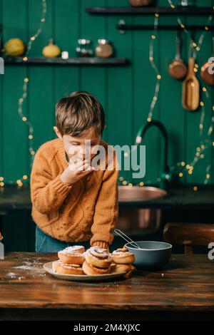 Garçon mangeant des petits pains à la cannelle dans la cuisine à Noël Banque D'Images