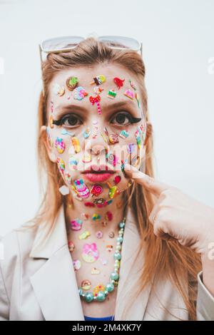 Femme avec des autocollants multicolores sur le visage contre fond blanc Banque D'Images