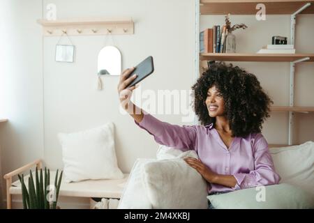 Femme souriante qui prend son selfie à la maison par téléphone portable Banque D'Images
