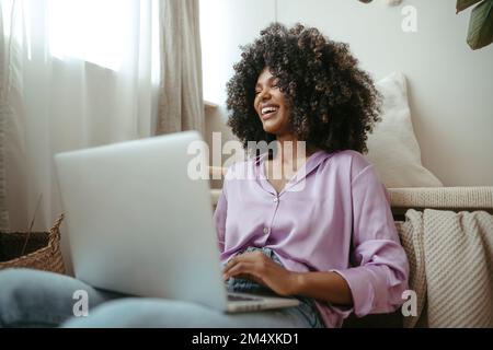 Jeune femme joyeuse avec ordinateur portable dans le salon Banque D'Images