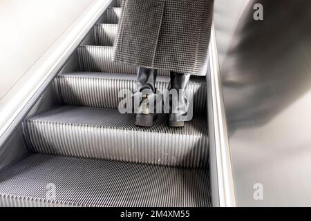 Vue arrière des pieds bottes en cuir et manteau d'hiver de femme sur l'escalier mécanique Elizabeth Line Farringdon station de métro Londres Angleterre Royaume-Uni KATHY DEWITT Banque D'Images