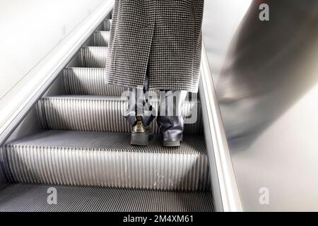 Vue arrière des pieds bottes en cuir et manteau d'hiver de femme sur l'escalier mécanique Elizabeth Line Farringdon station de métro Londres Angleterre Royaume-Uni KATHY DEWITT Banque D'Images