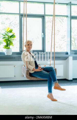 Femme d'affaires souriante assise sur le lieu de travail Banque D'Images