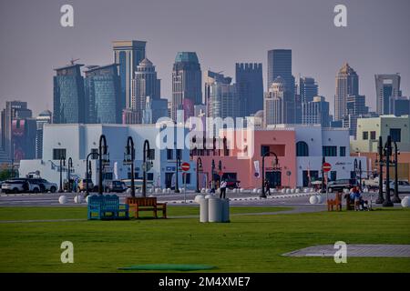 Le vieux port de Doha (district de Mina) à Doha, au Qatar, une prise de vue de l'après-midi montrant un bateau de croisière, des voitures et les gratte-ciel de Doha en arrière-plan avec les habitants et les visiteurs marchant Banque D'Images