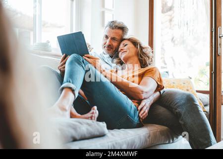 Couple d'âge mûr aimant utilisant un ordinateur tablette sur le canapé dans le salon Banque D'Images