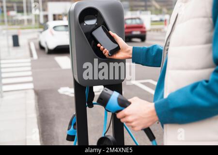 Homme qui balaie et paie par smartphone à la station de charge Banque D'Images