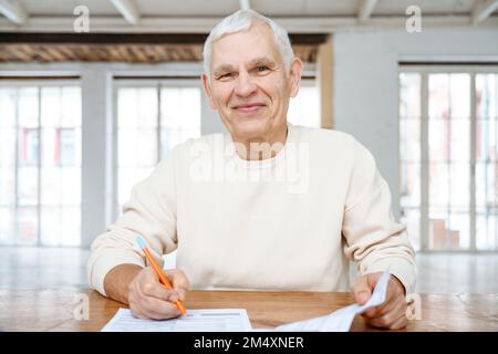 Homme senior souriant avec des factures financières à la maison Banque D'Images