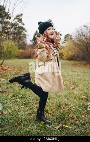 Bonne fille portant un chapeau en tricot montrant le signe de paix dans le parc Banque D'Images
