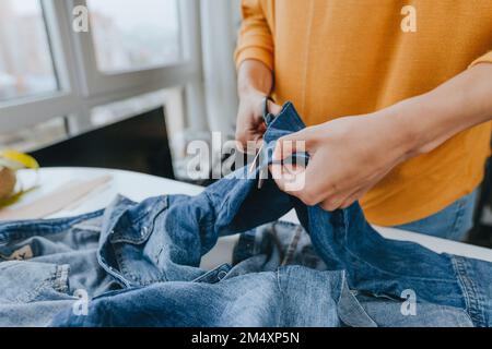 Mains de jeunes créateurs de mode coupant des jeans avec des ciseaux dans l'atelier Banque D'Images