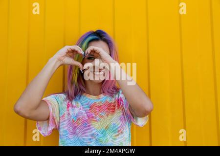 Bonne femme en forme de coeur avec les mains devant le mur jaune Banque D'Images