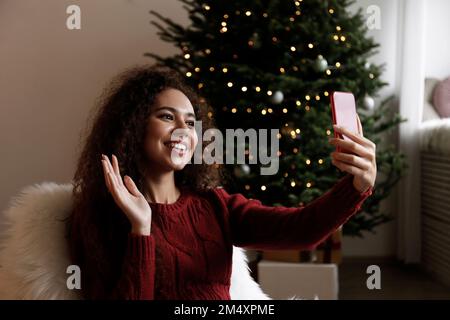 Une jeune femme heureuse qui parle lors d'un appel vidéo et qui agite sur un smartphone Banque D'Images