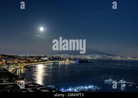 Vue sur le golfe de Naples en Italie, le front de mer en premier plan et le Vésuve en arrière-plan. La pleine lune s'élève au-dessus de l'horizon. Banque D'Images