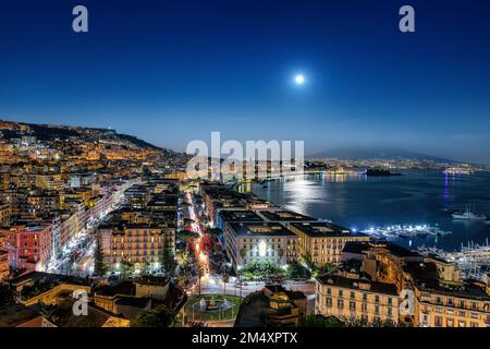 Vue sur le golfe de Naples en Italie, avec les palais de bord de mer en premier plan et le Vésuve en arrière-plan. La pleine lune s'élève au-dessus de l'horizontale Banque D'Images