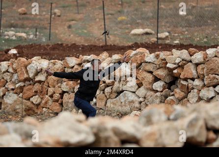 Naplouse, Palestine. 23rd décembre 2022. Un manifestant palestinien utilise un coup de feu pour lancer une pierre lors d'affrontements avec des soldats israéliens à la suite d'une protestation contre l'expansion des colonies juives dans le village de Beit Dajan, en Cisjordanie, à l'est de Naplouse, le 23 décembre 2022. Credit: Ayman Nobani/Xinhua/Alamy Live News Banque D'Images