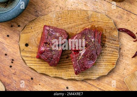 Préparation du steak de filet de bœuf cru sur une planche de bois avec sel de mortier et poivre, sorbets et romarin frais photographiés du côté. Banque D'Images