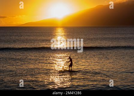 Un homme sur un paddle-board au coucher du soleil à Napili Bay, Maui, Hawaii. Banque D'Images