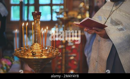 Des bougies allumées sur le fond du prêtre lisant la Bible au service. Banque D'Images