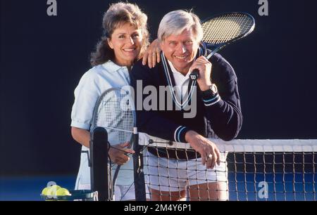 Couple plus âgé vêtus d'une tenue de tennis, s'arrêtant pour prendre une photo tout en se penchant sur le filet et tenant une raquette Banque D'Images