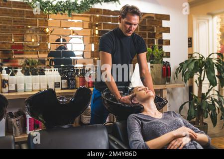 Une jeune femme se lavoir au salon par un coiffeur professionnel. Prise de vue en intérieur moyenne. Soins capillaires. Photo de haute qualité Banque D'Images